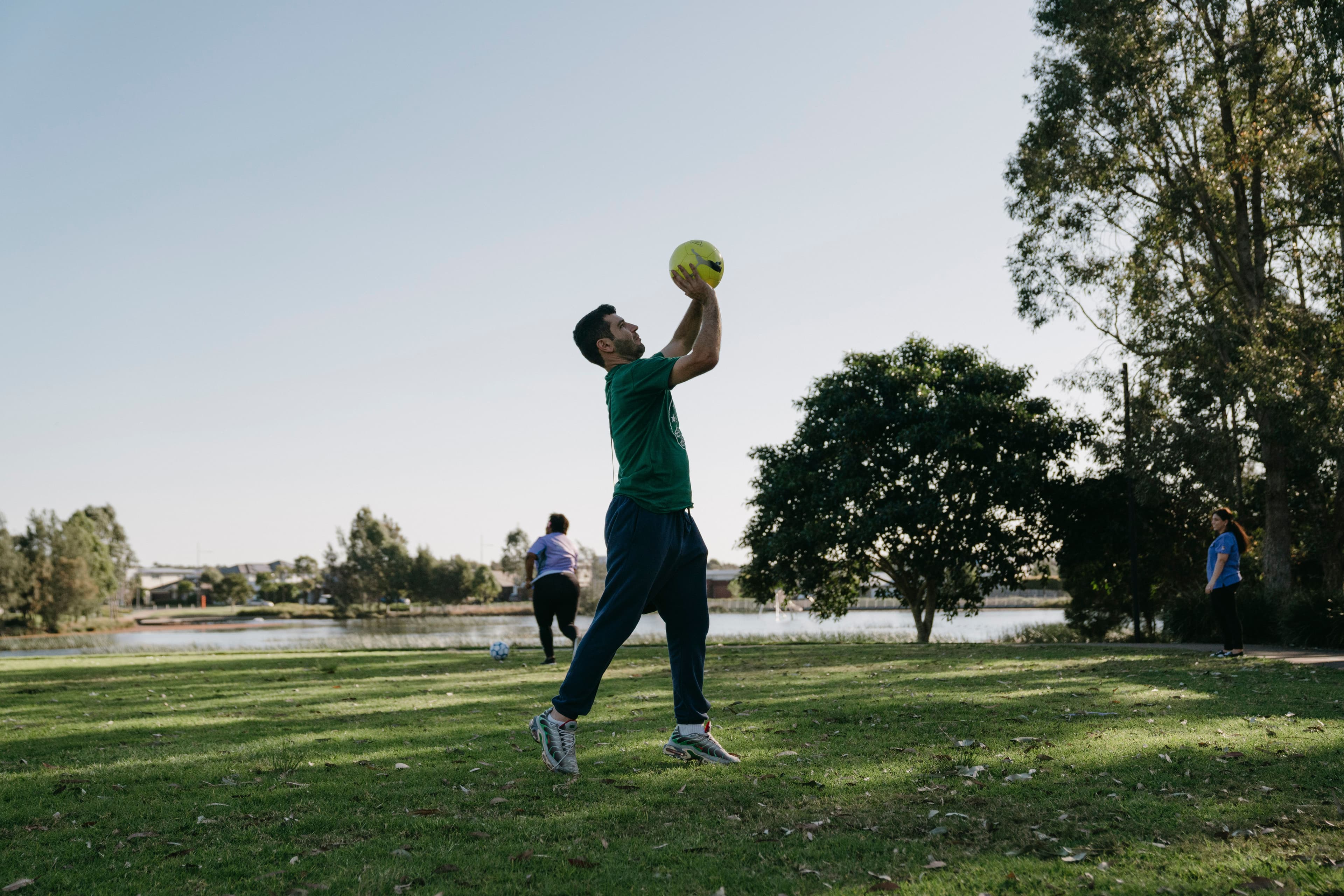 Mark, who lives with a disability, is getting out of his comfort zone and jumps to reach for a ball that has been thrown at him in a park in some shade