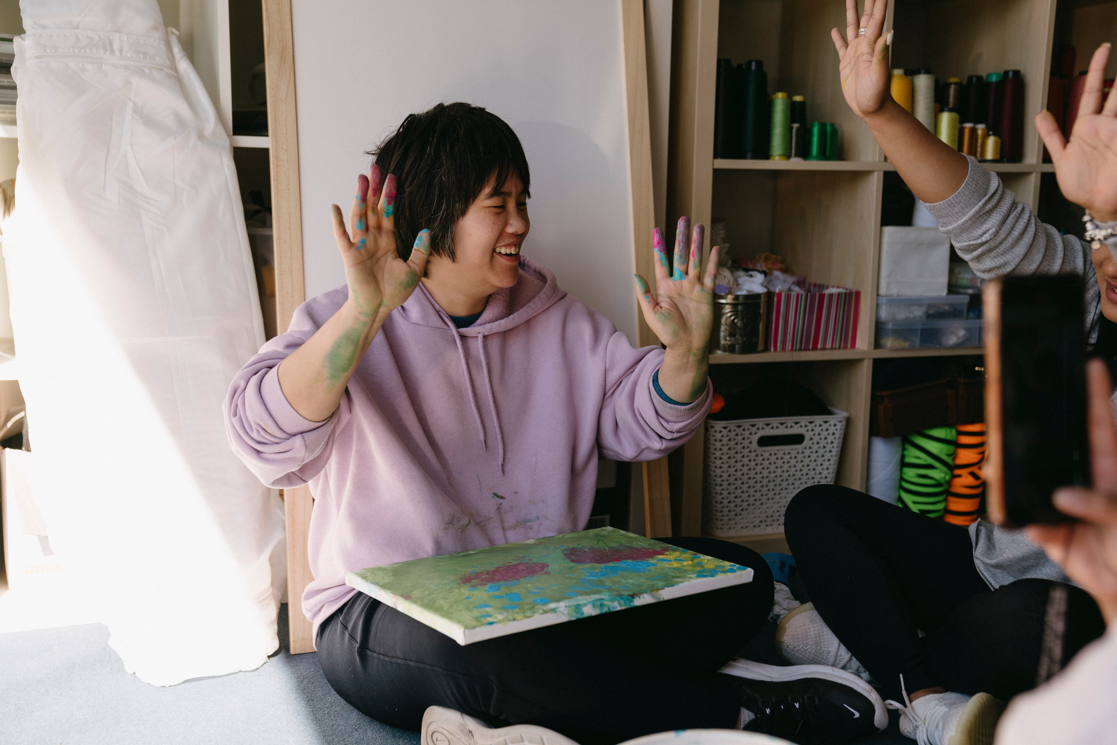 Melissa is smiling and plaching her hands in the air as she was finger painting on canvas