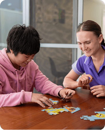 A Bopha Cares disability worker smiling and playing a game of puzzles with Melissa who is also smiling and enjoying herself